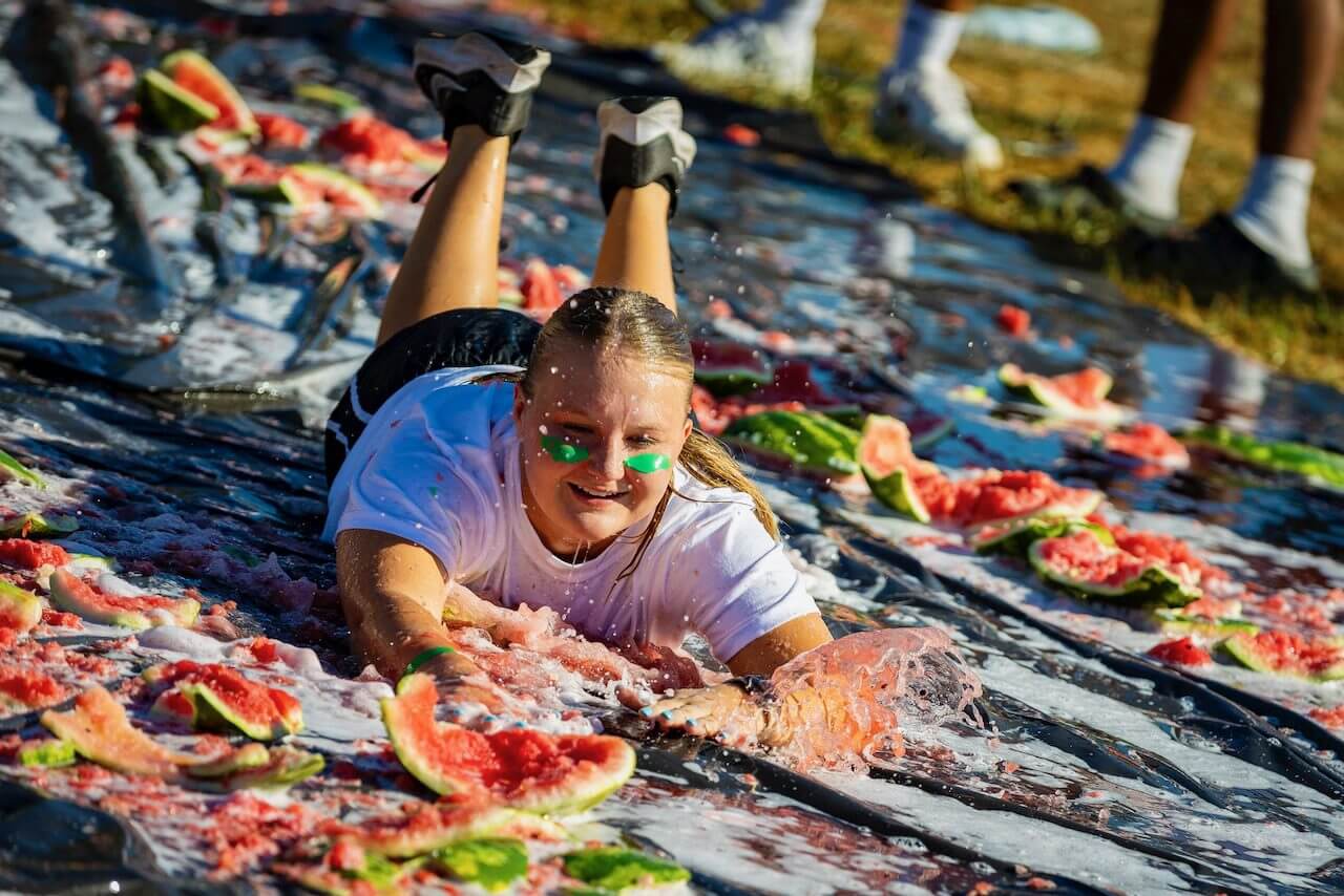 Person sliding on watermelon-covered tarp outdoors.