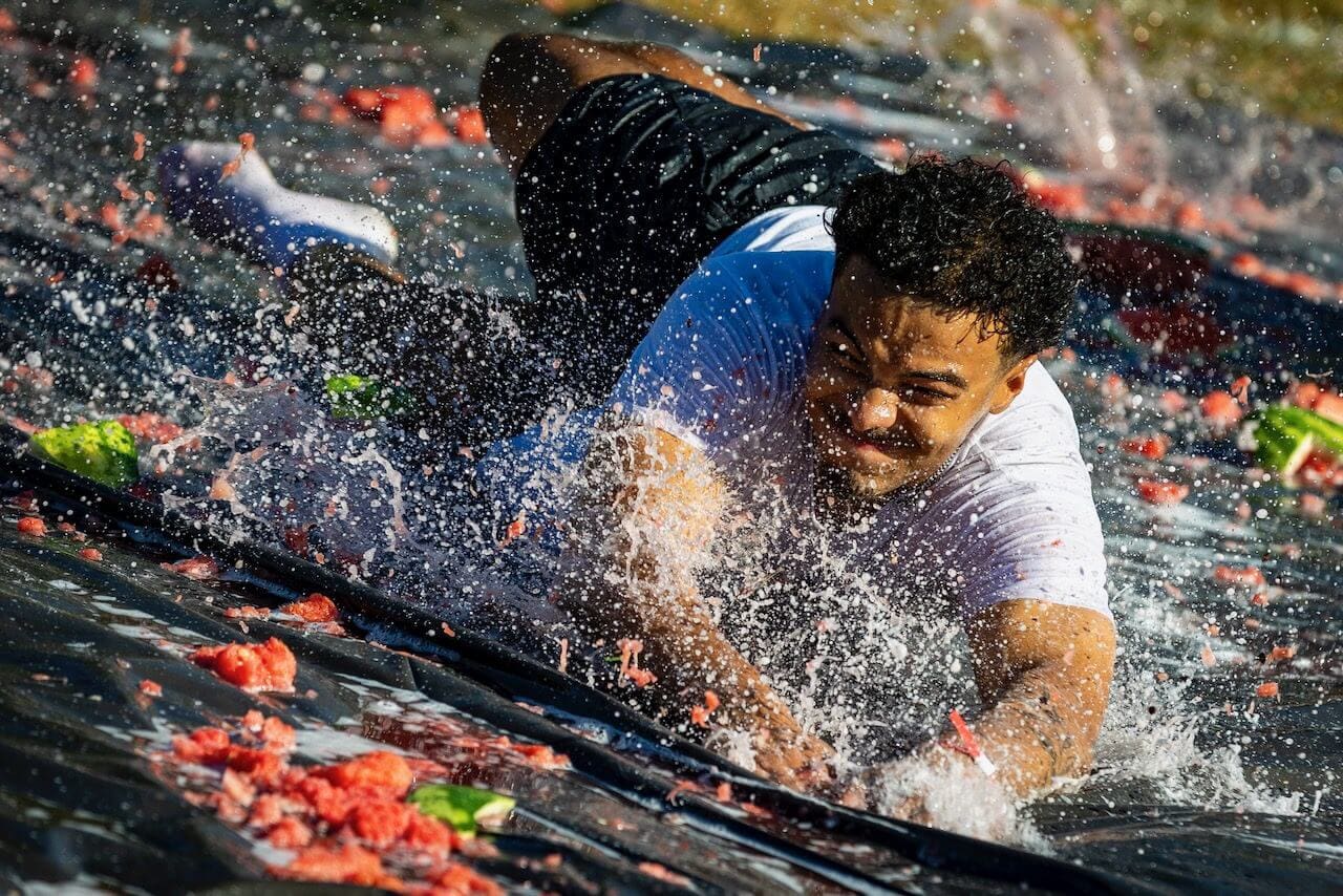 Man sliding on wet tarp with watermelons.