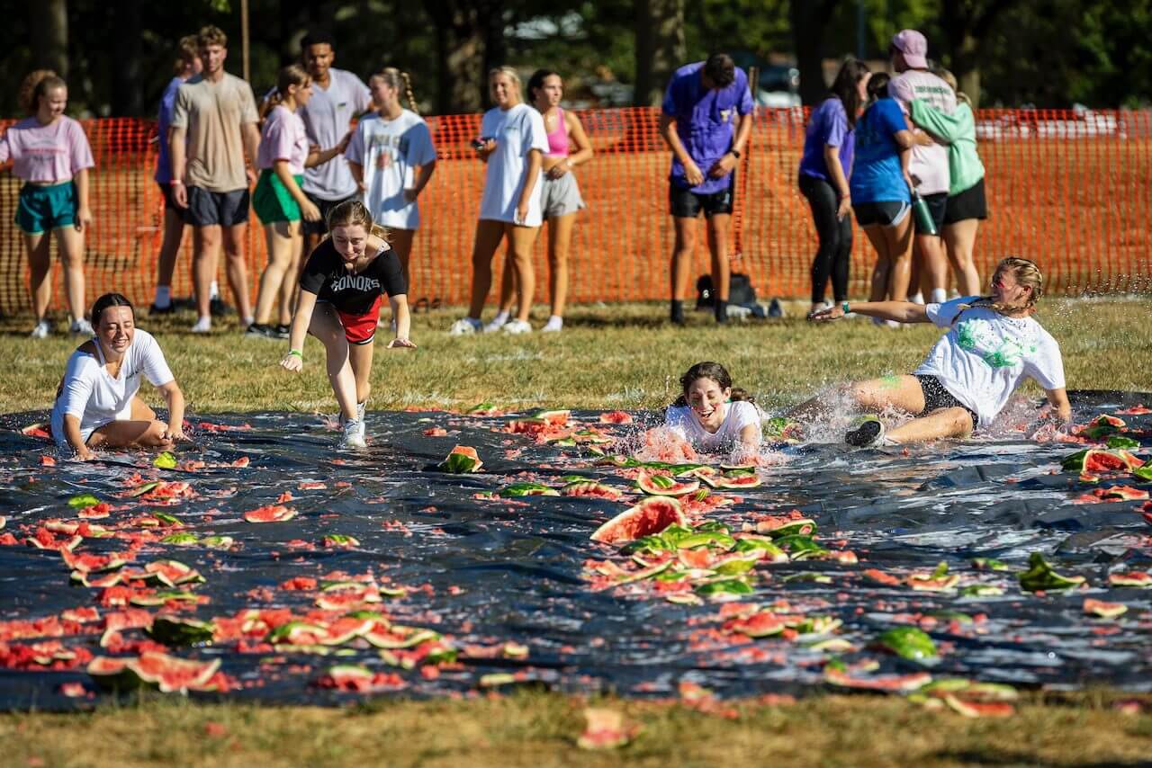People sliding on watermelon-covered tarp outdoors.