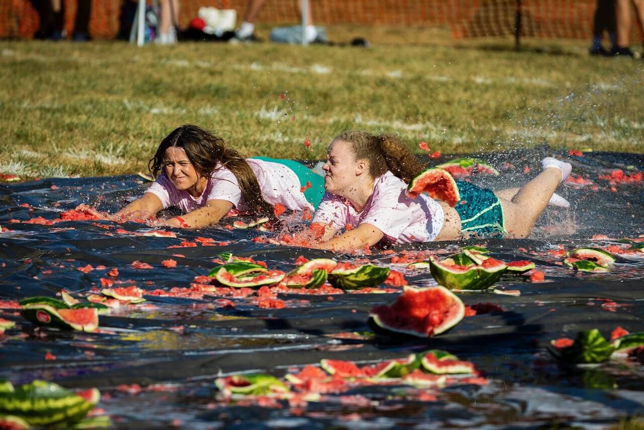 People sliding on watermelon-covered tarp outdoors.