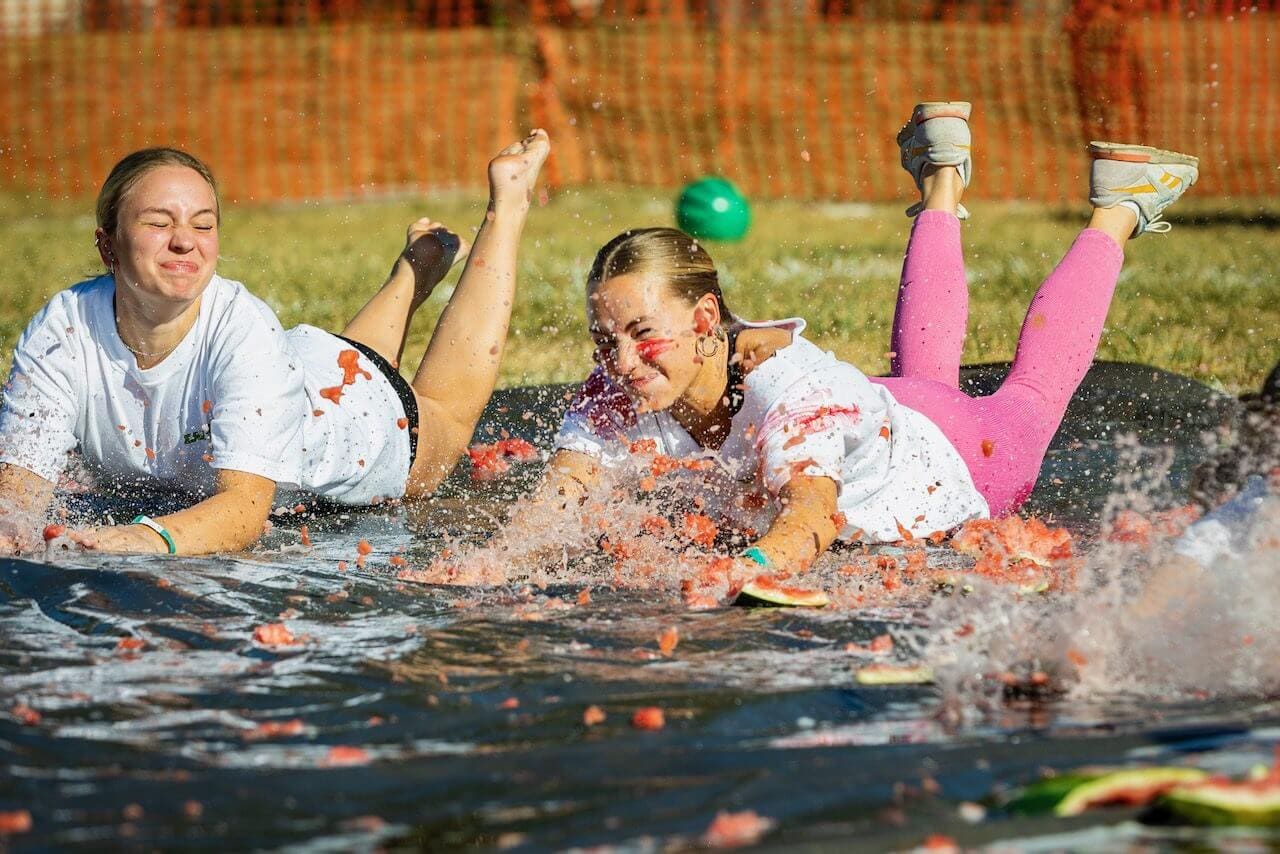 People sliding on watermelon-covered tarp outdoors.