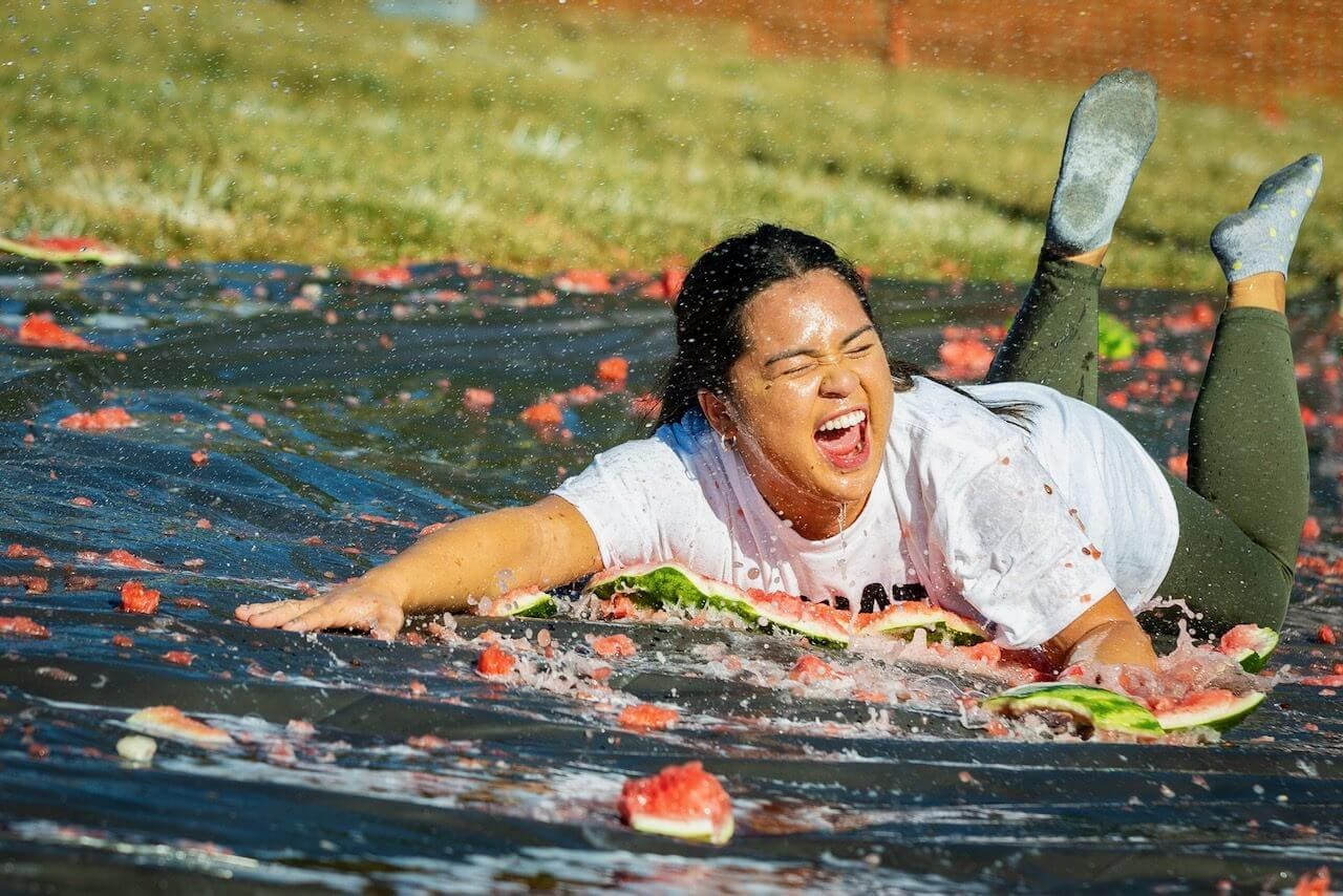 Person sliding on watermelon-covered tarp, smiling.