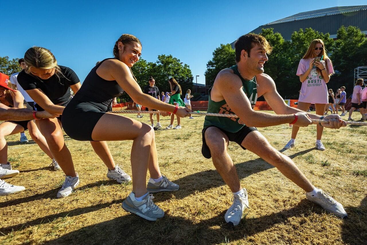 People playing tug-of-war on grass field.