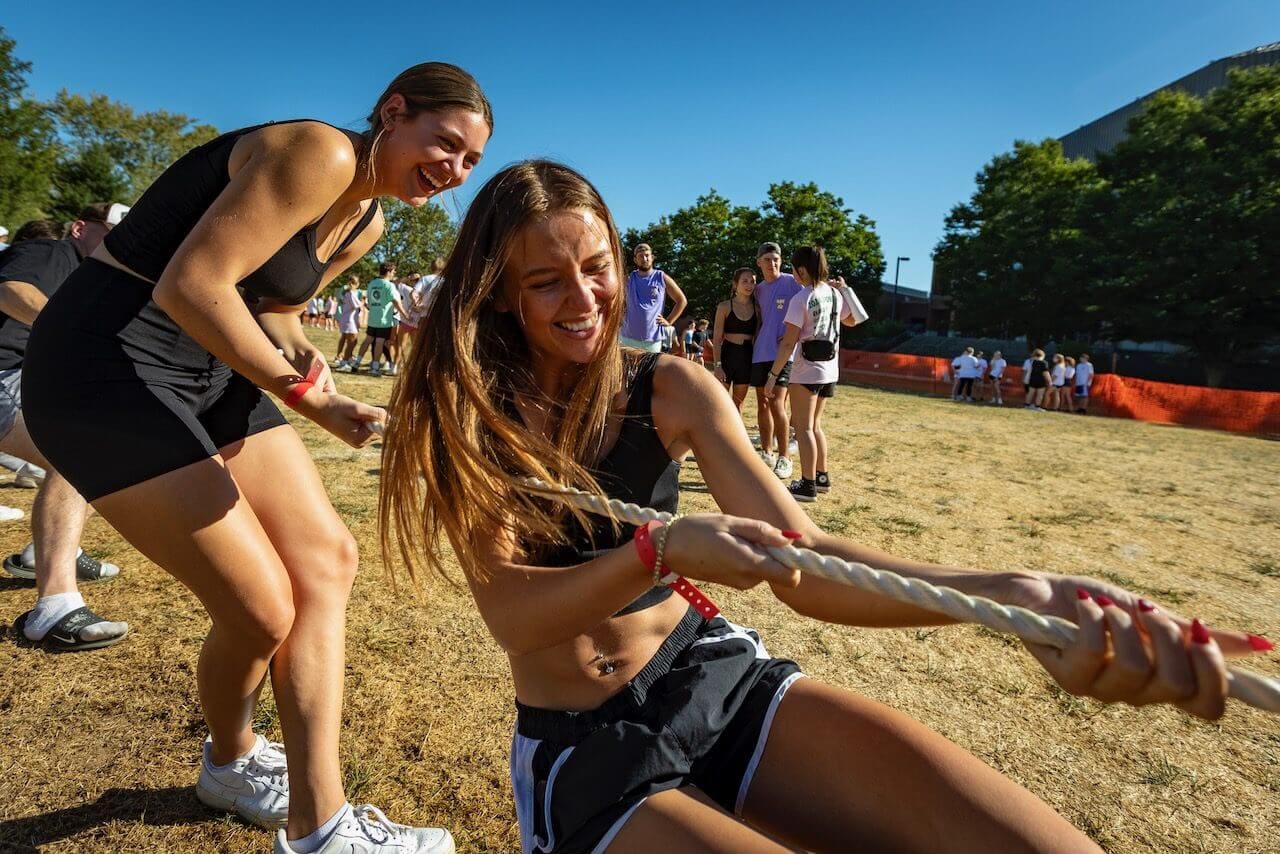 Women playing tug-of-war outdoors, smiling.
