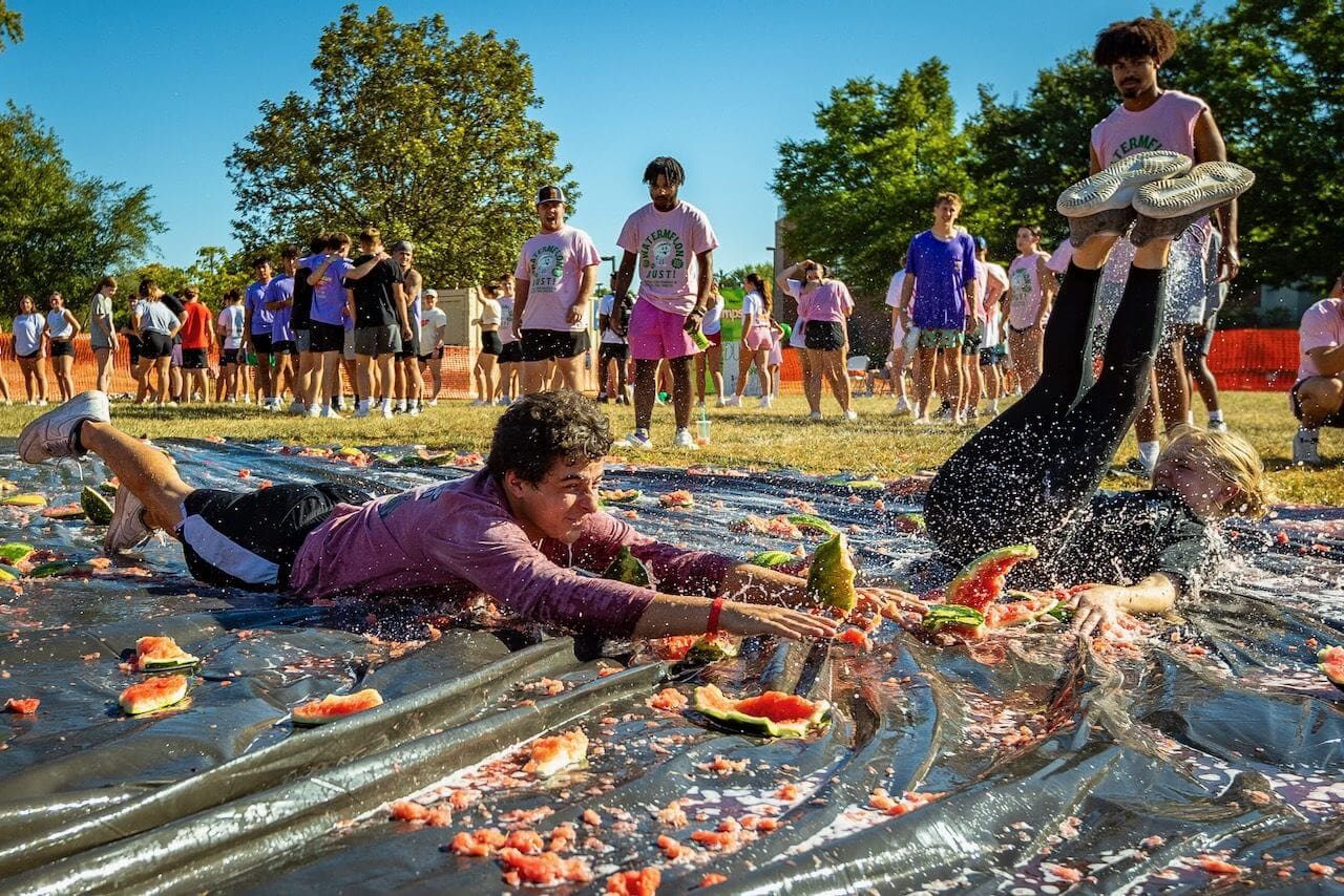 People sliding on watermelon-covered tarp outdoors.