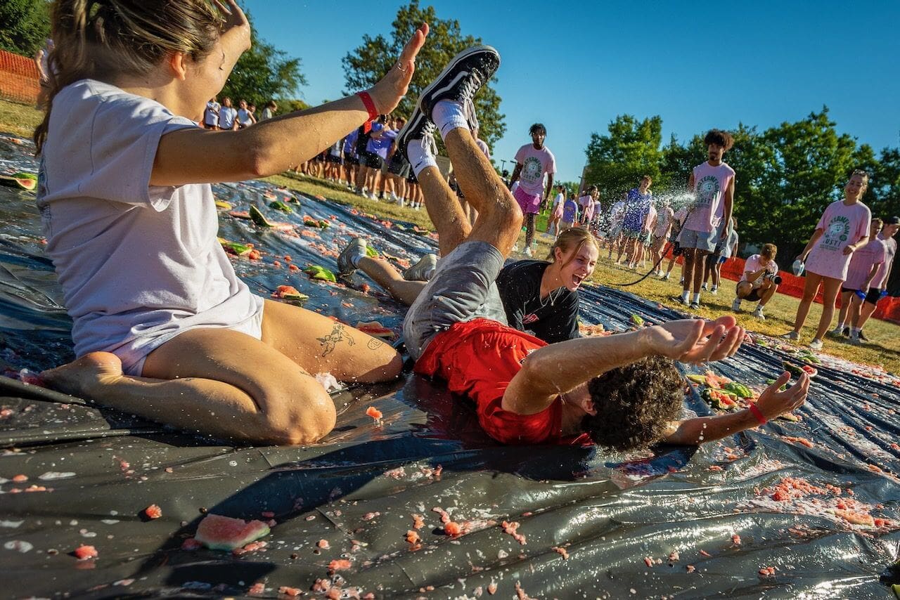People sliding on watermelon-covered tarp outdoors.