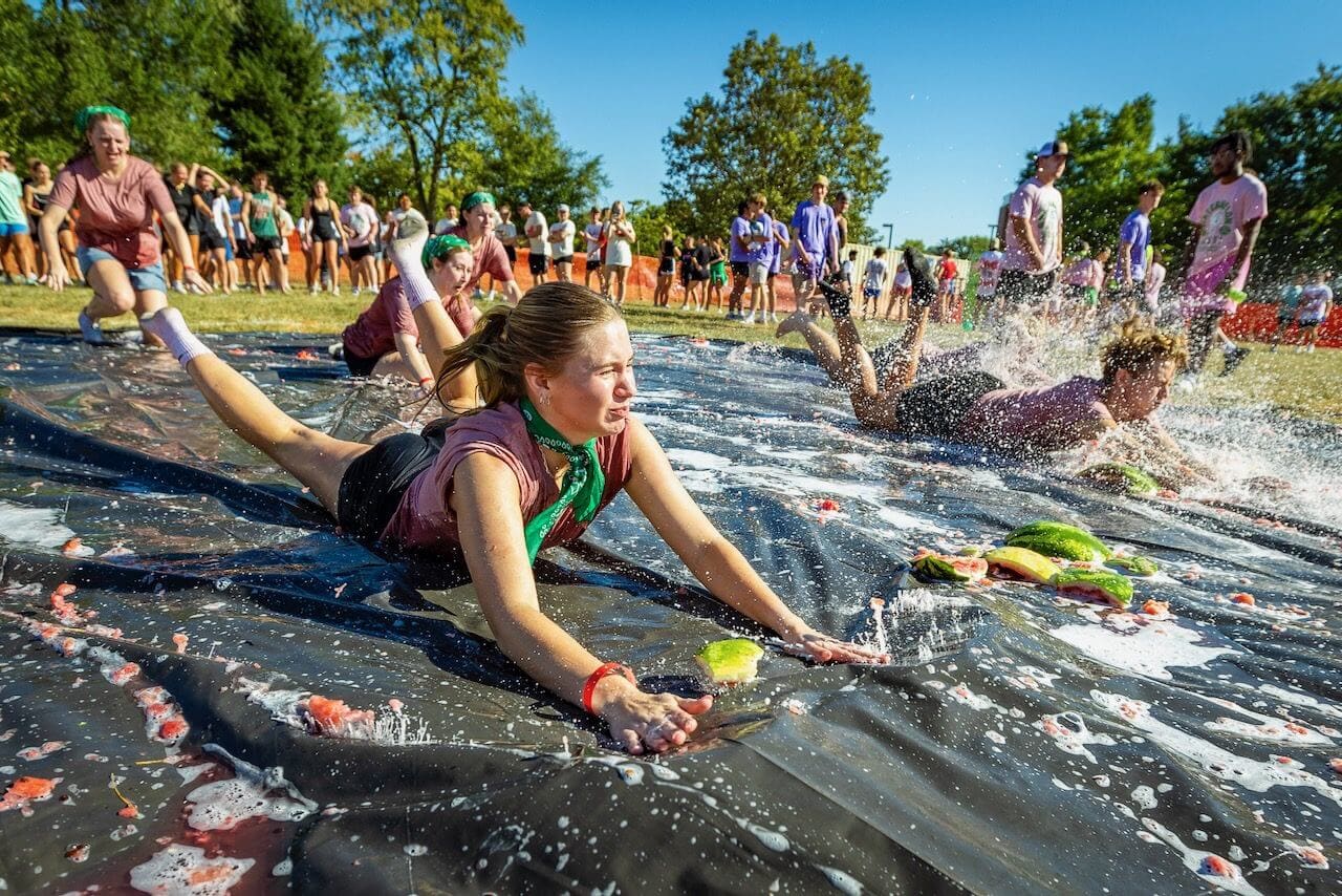 People sliding on soapy tarp outdoors event.