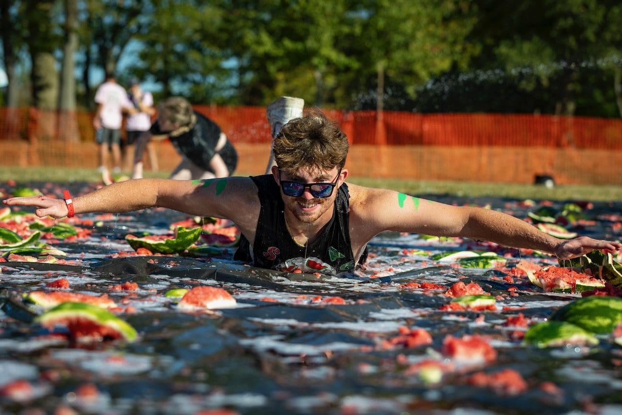 Man sliding on watermelon-covered tarp outdoors.