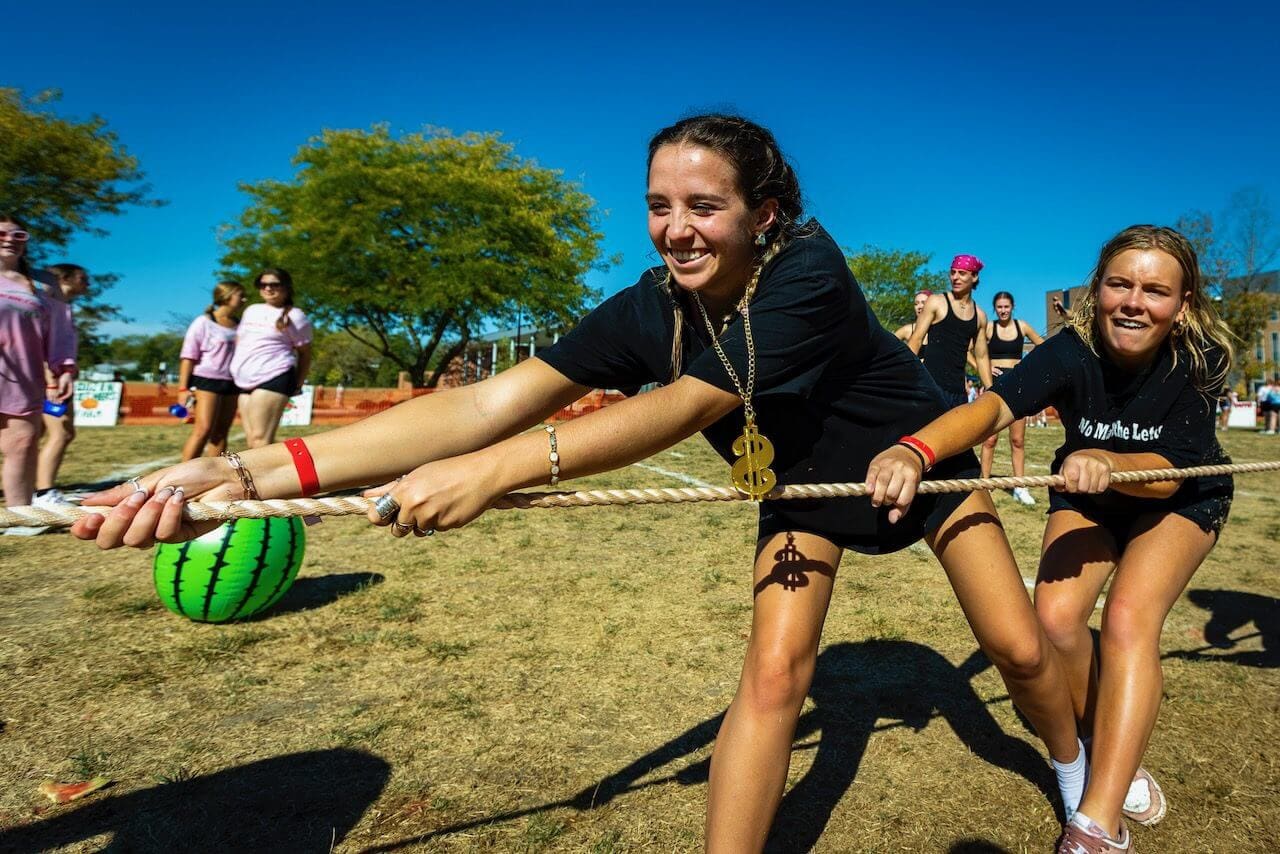 Girls playing tug-of-war outdoors, smiling.