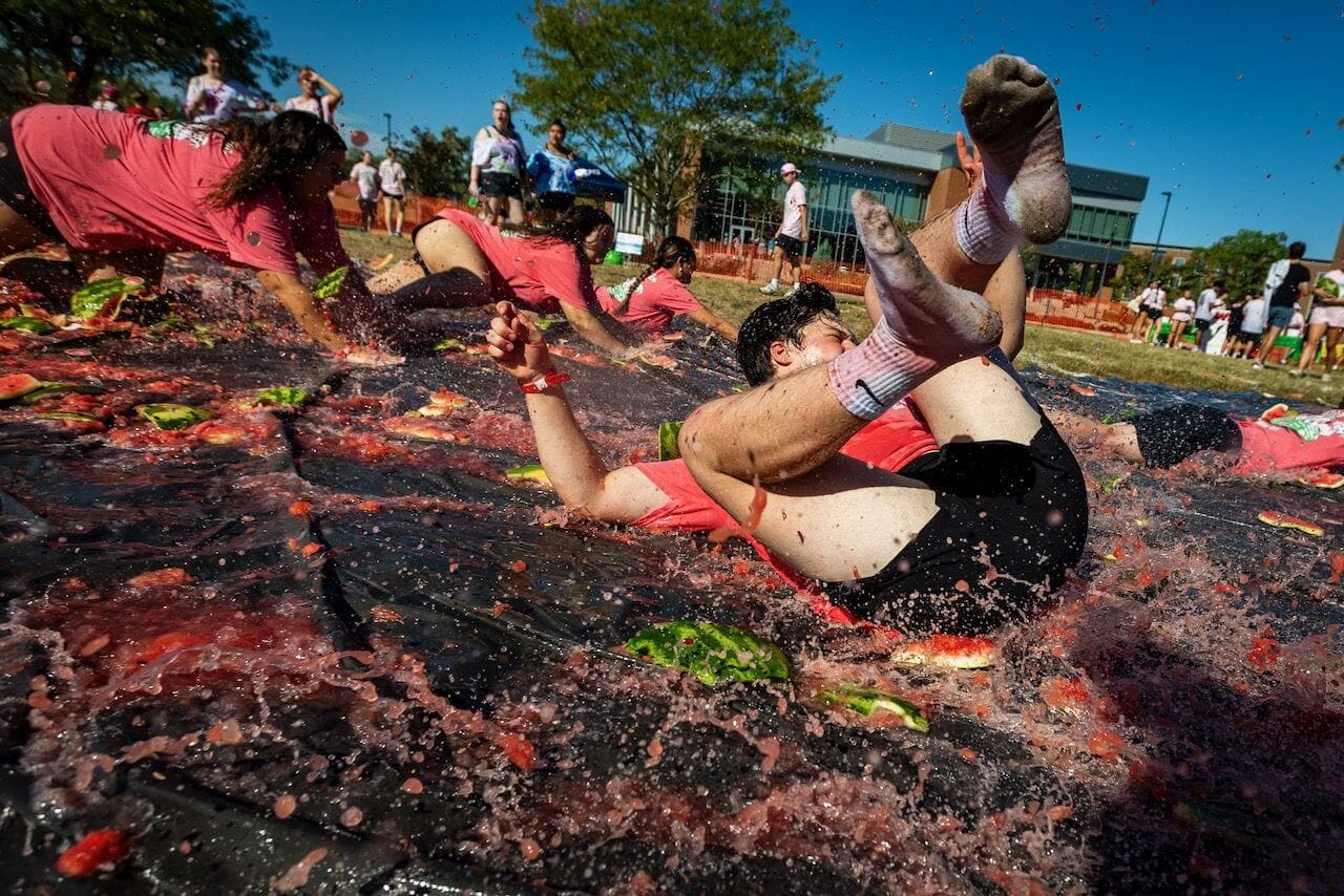 People sliding through smashed watermelons on tarp.