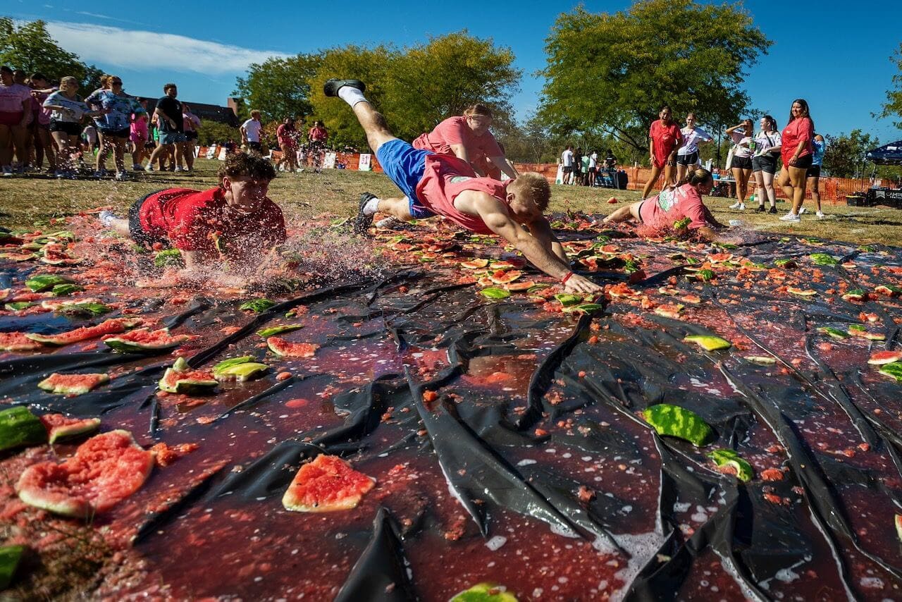 People sliding on watermelon-covered tarp outdoors.